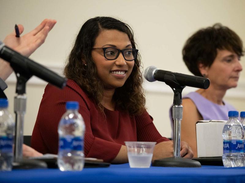 Woman of color seated on a panel with other women