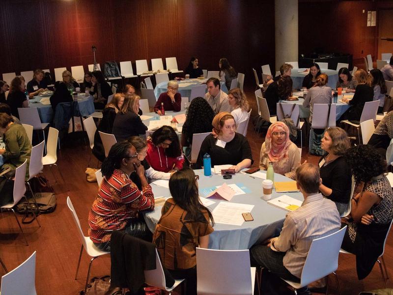 Dozens of women seated at conference tables, speaking avidly to one another